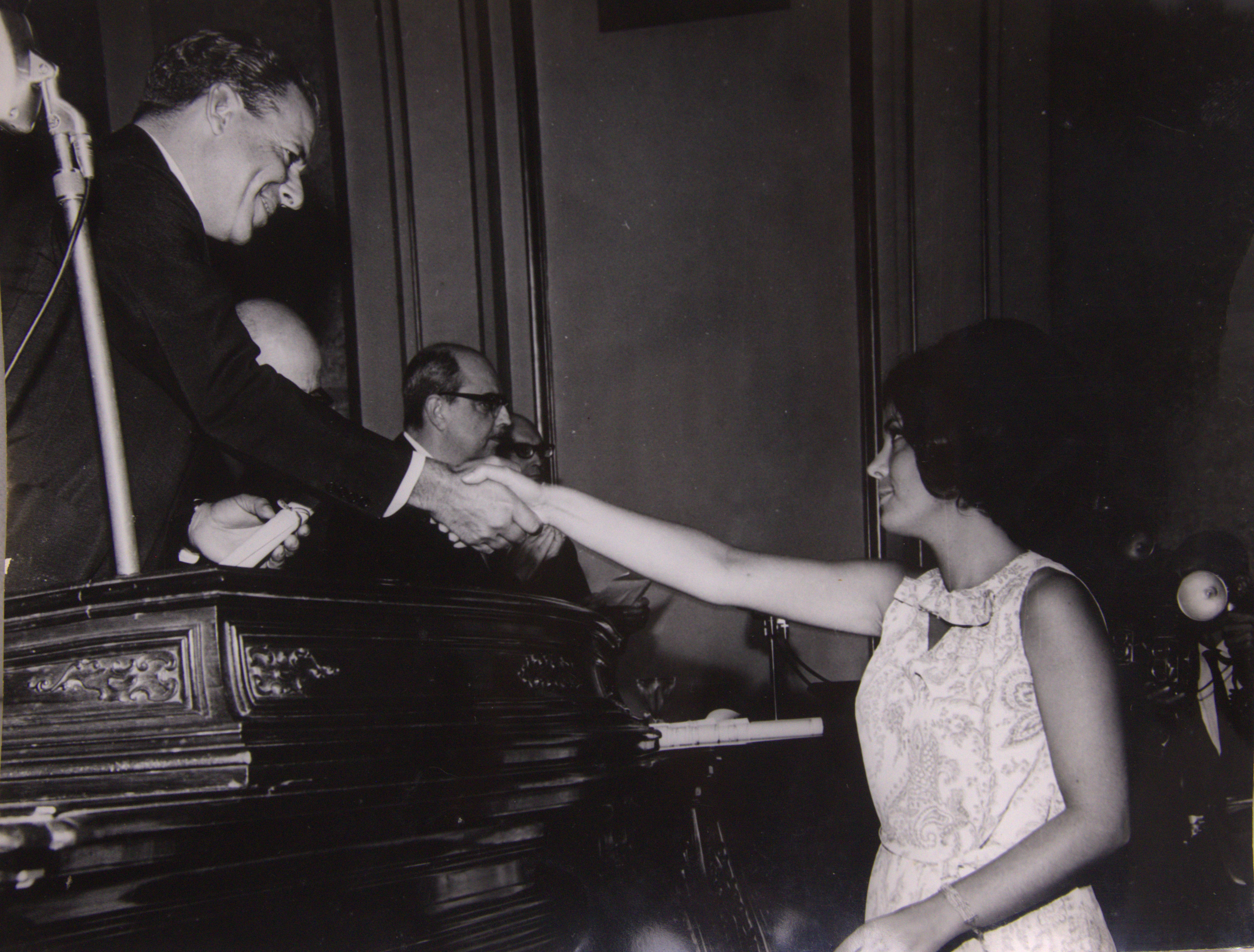 Foto feita durante a cerimônia de formatura de Heloisa Vilhena, após a conclusão do curso preparatório no Instituto Rio Branco. Ela cumprimenta o então presidente da República João Goulart. Ao fundo, também aparece na foto o ex-chanceler San Tiago Dantas, eleito paraninfo da turma de formandos da qual Heloisa fez parte.